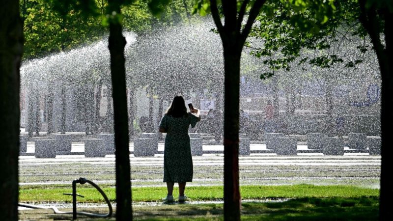 A woman stands on August 27, 2024 in front of a sprinkler watering the lawn close to the Chancellery in Berlin, where temperatures were expected to reach up to 30 degrees Celsius during the following days. (Photo by Tobias SCHWARZ / AFP)